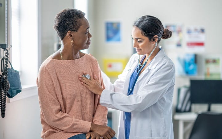 Female doctor checking woman's heartbeat with stethoscope