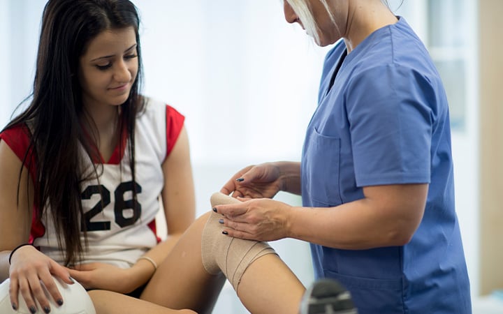 A nurse applying a bandage to the inured knee of a female volleyball player