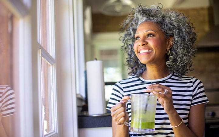 A happy middle-aged woman drinks coffee in her kitchen