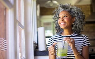 A happy middle-aged woman drinks coffee in her kitchen