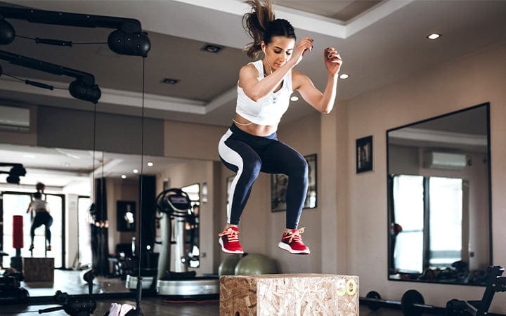 A woman jumping on a box in the gym