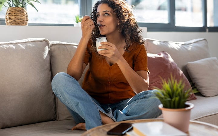 A young woman eating yogurt on her sofa at home