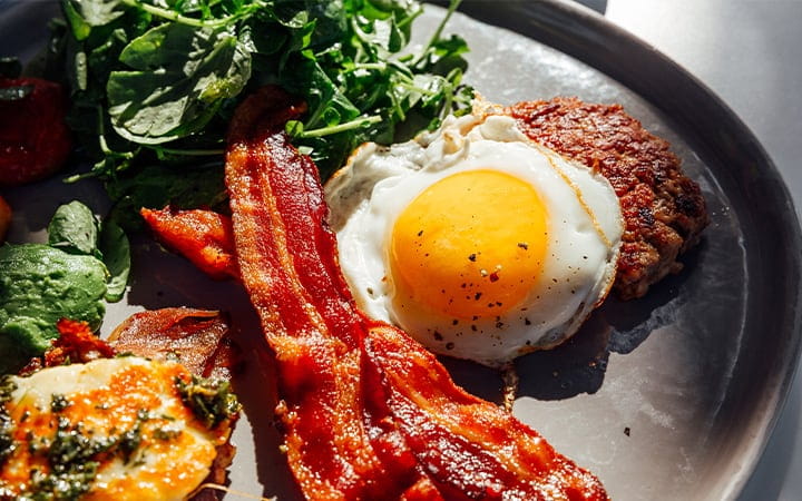 Keto breakfast with fried egg, bacon, cheese, ground beef and salad