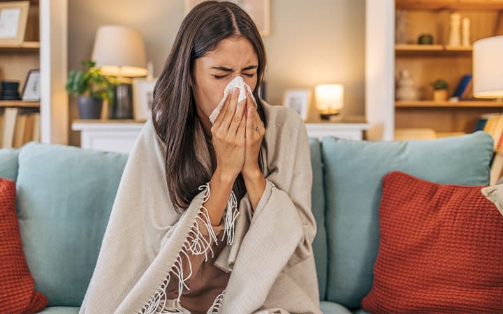 woman on couch blowing her nose