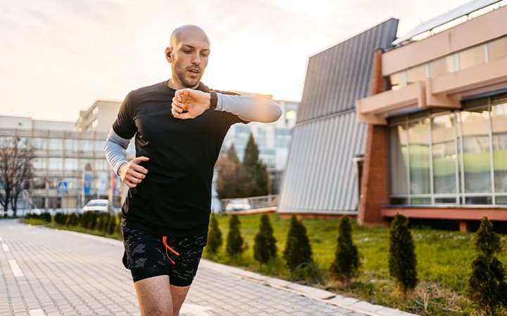 A young athlete checking fitness activity on smartwatch while running outdoors