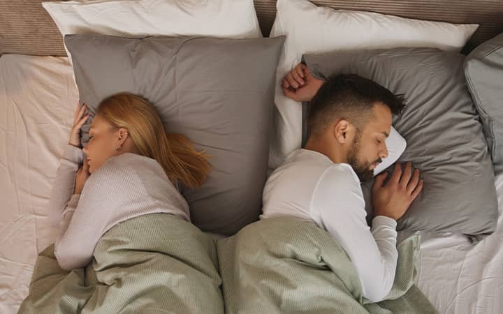 A young couple sleeping in bed back to back