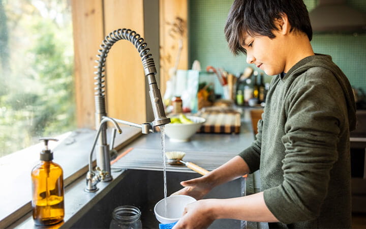 A teenage boy washing dishes in a kitchen