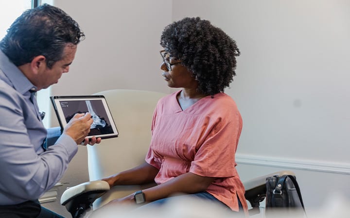 A female patient sits with her podiatrist to review her x-ray and discuss new treatment options