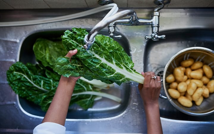 woman rinses leafy greens in kitchen sink
