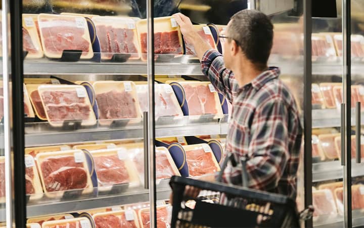 Male customer with a shopping basket taking meat from a fridge at local supermarket