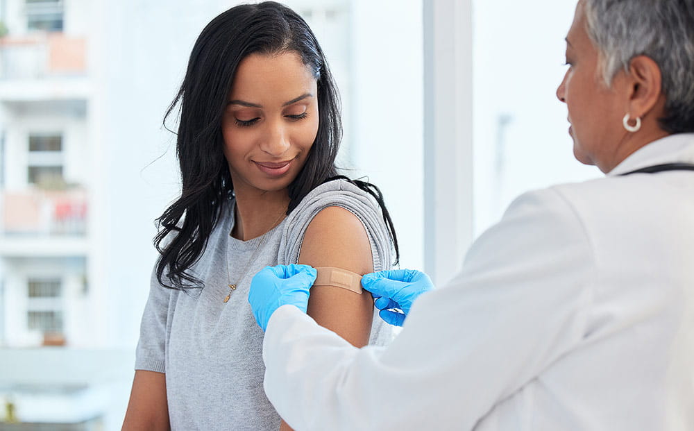 A provider applies a bandage to her female patient after a vaccination