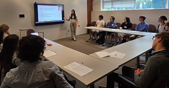 Student is presenting in front of slide screen during the Health Services Research Center Summer Scholar Program 2025.
