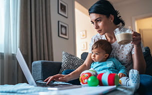 Young modern mother with a baby using laptop at home