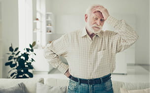 Close up photo of grey haired man holding his head