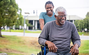A senior man in a wheelchair is pushed around by his daughter