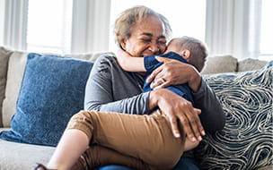 Grandmother embracing toddler grandson on couch and laughing
