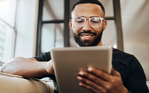 Young africa american man smiling on the couch using a tablet at home.