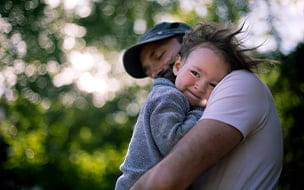 2 year old is being held by dad while the wind messes with his hair