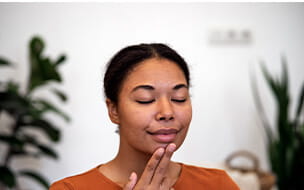 Happy calm African American woman using EFT tapping, touching face with fingertips, to relieve stress and anxiety