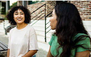 Two young women sitting on the bench and talking outdoors