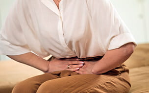 Mature woman sitting on sofa in living room at home and suffering from abdominal pain.