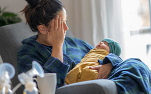 A new mother sitting on a rocking chair holding her newborn baby with a breast pump near by.
