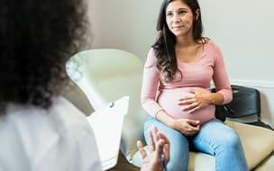 Expectant mother touches abdomen while listening to unrecognizable doctor
