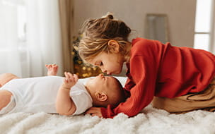 Adorable child kissing little sister lying on white bedding