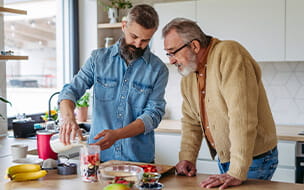 Senior father and mature son making fruit smoothie as snack.