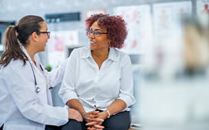 African American woman smiles as she discusses with the doctor sitting beside her.