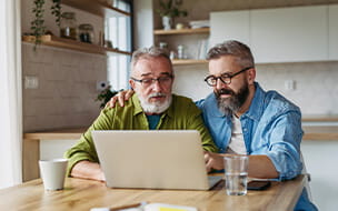 Mature son teaching father to work with internet at the kitchen table.