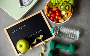 New Year for New Health sign with an apple and tape messure along with a fresh vegetable salad, scale, and dumbells