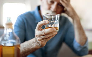 Man drinking home alone staring at a glass with alcohol he's holding