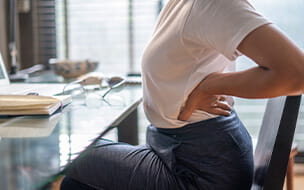 Woman in home office suffering from back pain sitting at computer desk