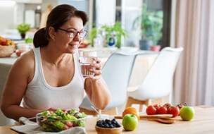 Woman drinking water while having a healthy meal at kitchen table