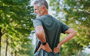 Senior men walking outside clenching his back in pain