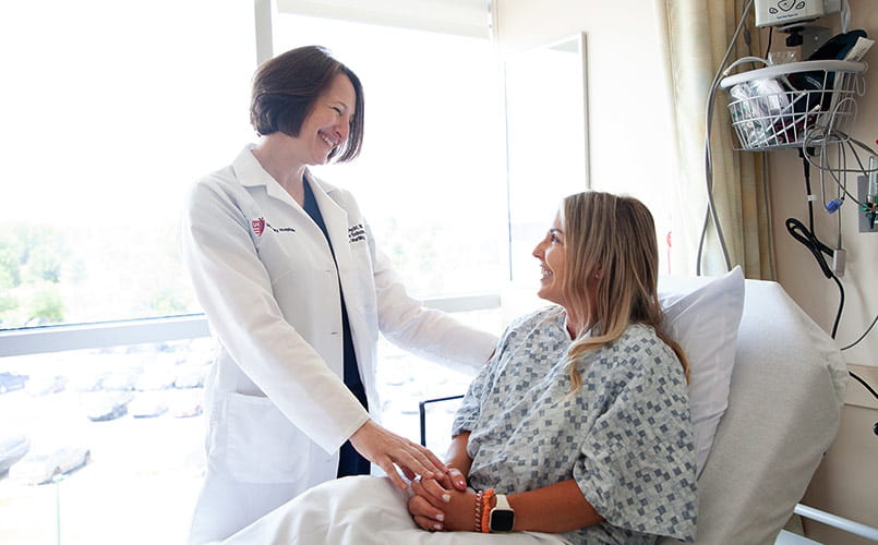 A doctor is talking to a patient in hospital gown in a hospital bed