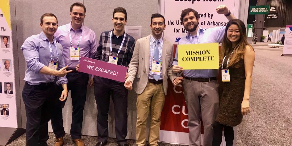 Group of 6 radiology residents standing in a row holding signs we escaped and mission complete