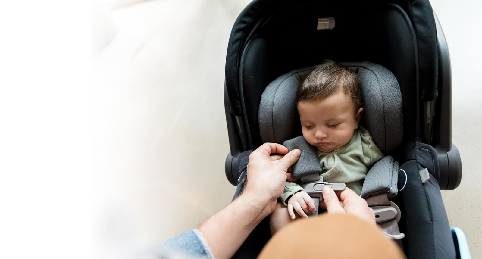 A parent buckling their newborn baby boy into a car seat.