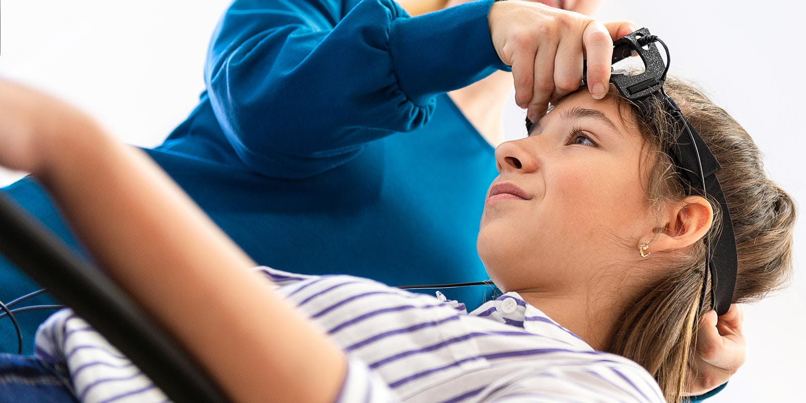 A young girl leans back to have a biofeedback sensor placed on her head
