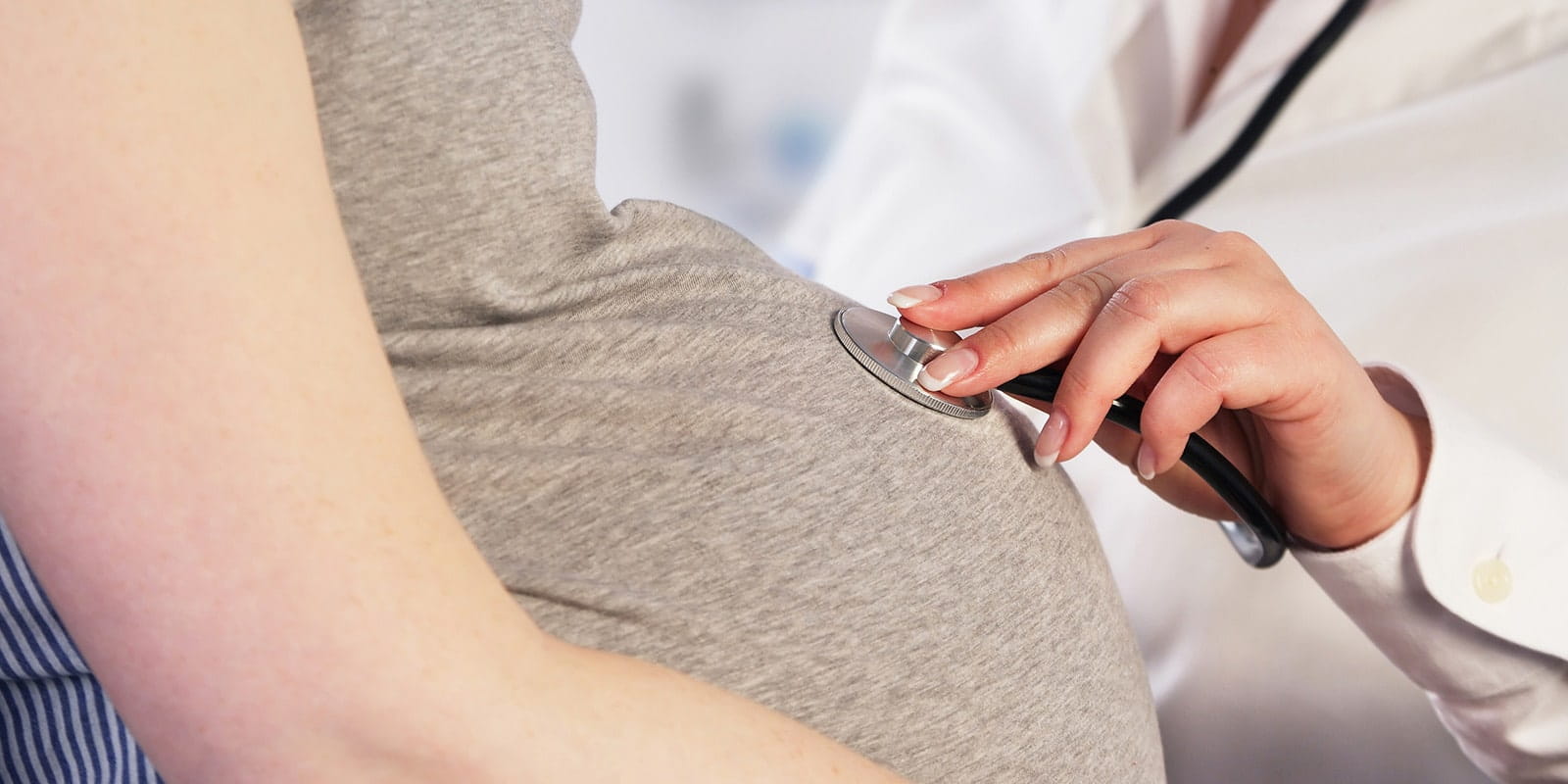 Doctor listening to unborn baby's heartbeat in pregnant woman.