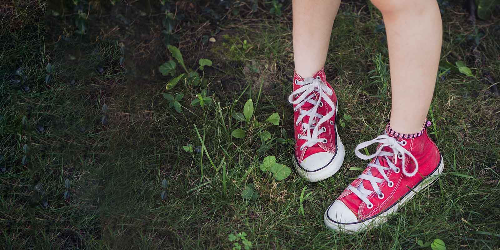Legs of girl in red canvas shoes on the grass