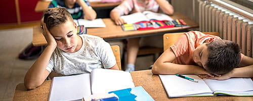 Two sleep-deprived school kids sitting in the classroom