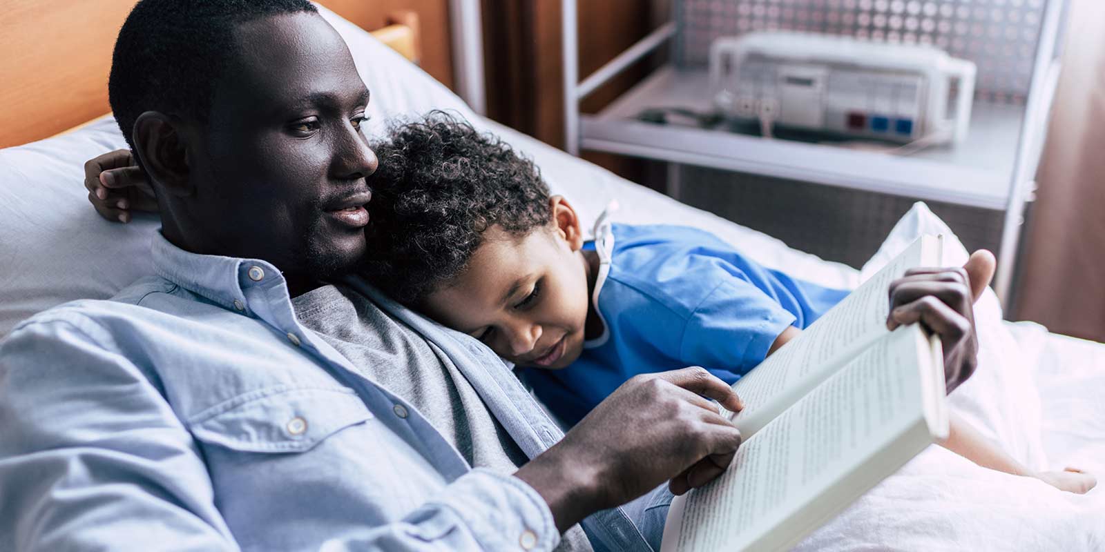 Father and son in hospital bed reading together.