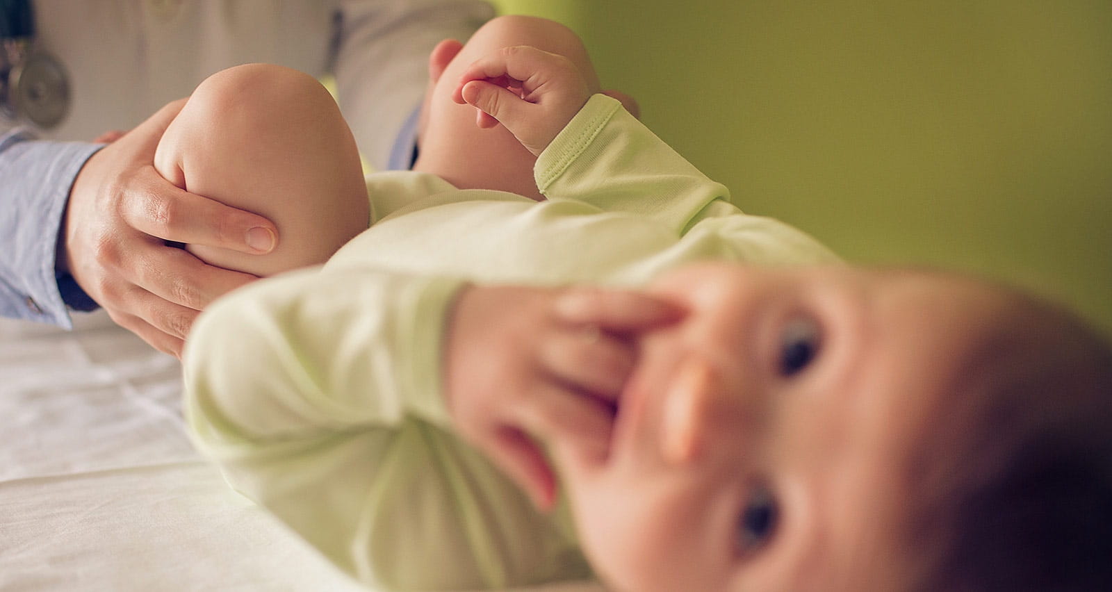 A baby boy lying down at the doctor's office as a female doctor examining him