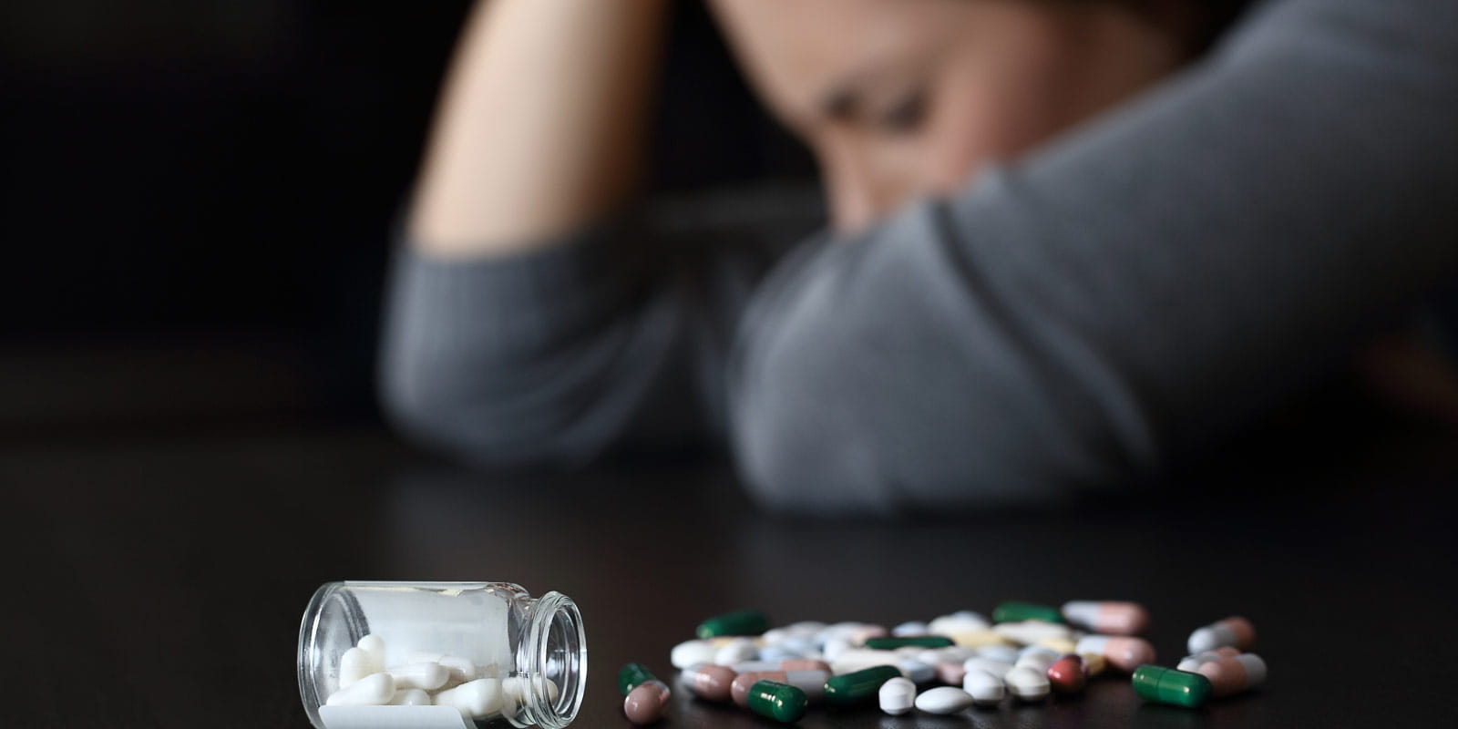 A distraught woman sits beside a spilled bottle of pills