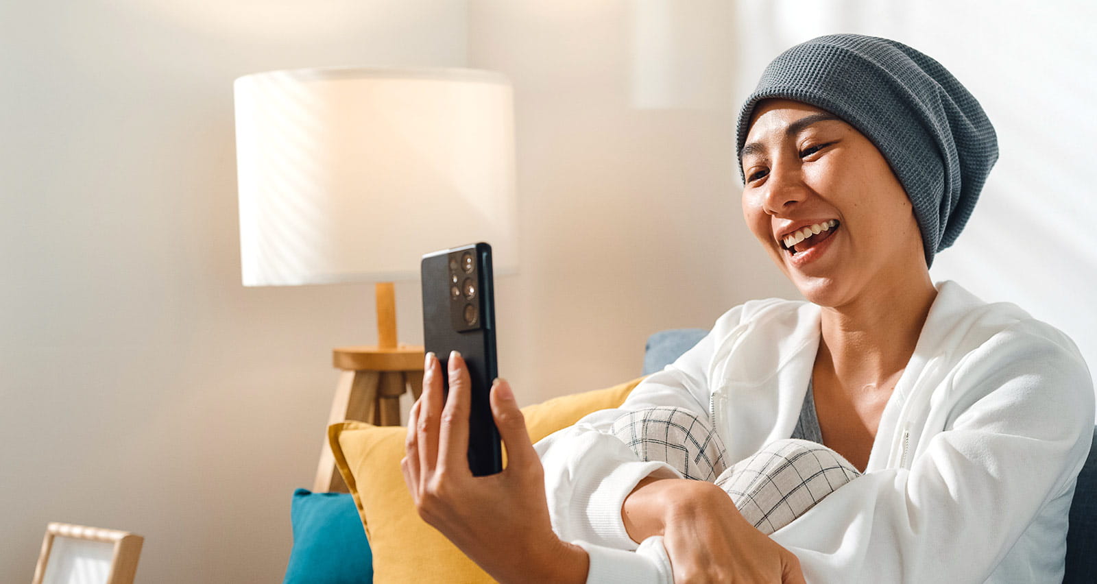Young woman recovering from cancer using phone talk to friends while sitting on a sofa in her living room