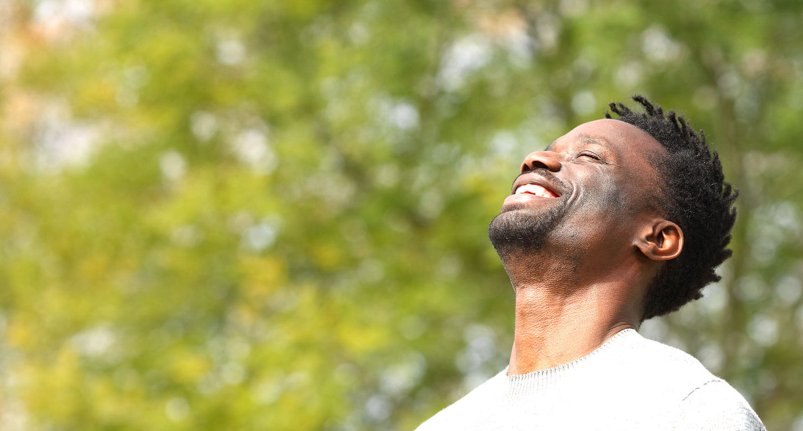 A smiling man closes his eyes as he takes in a sunny day outdoors