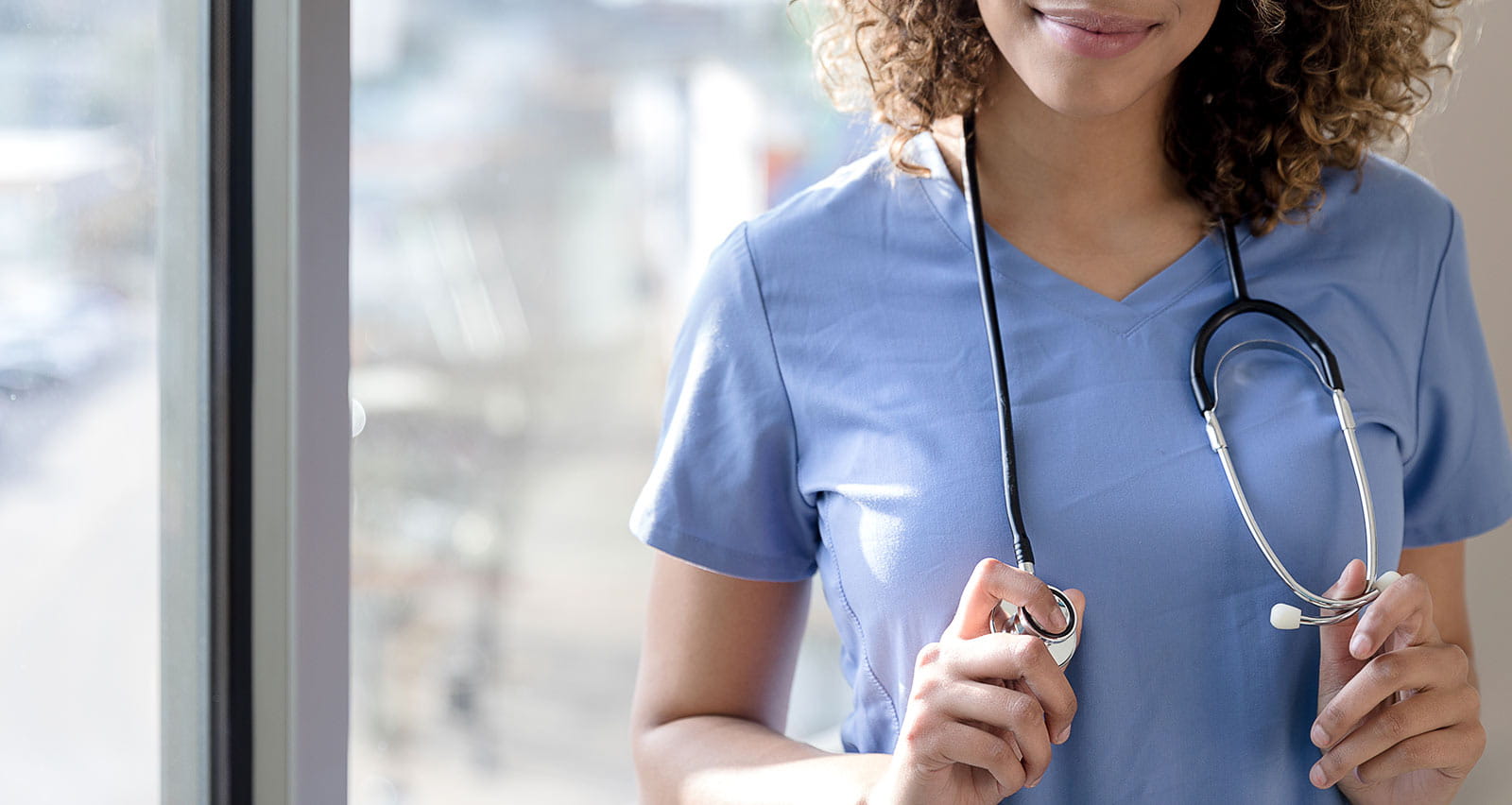A smiling female doctor wearing scrubs with a stethoscope around her neck