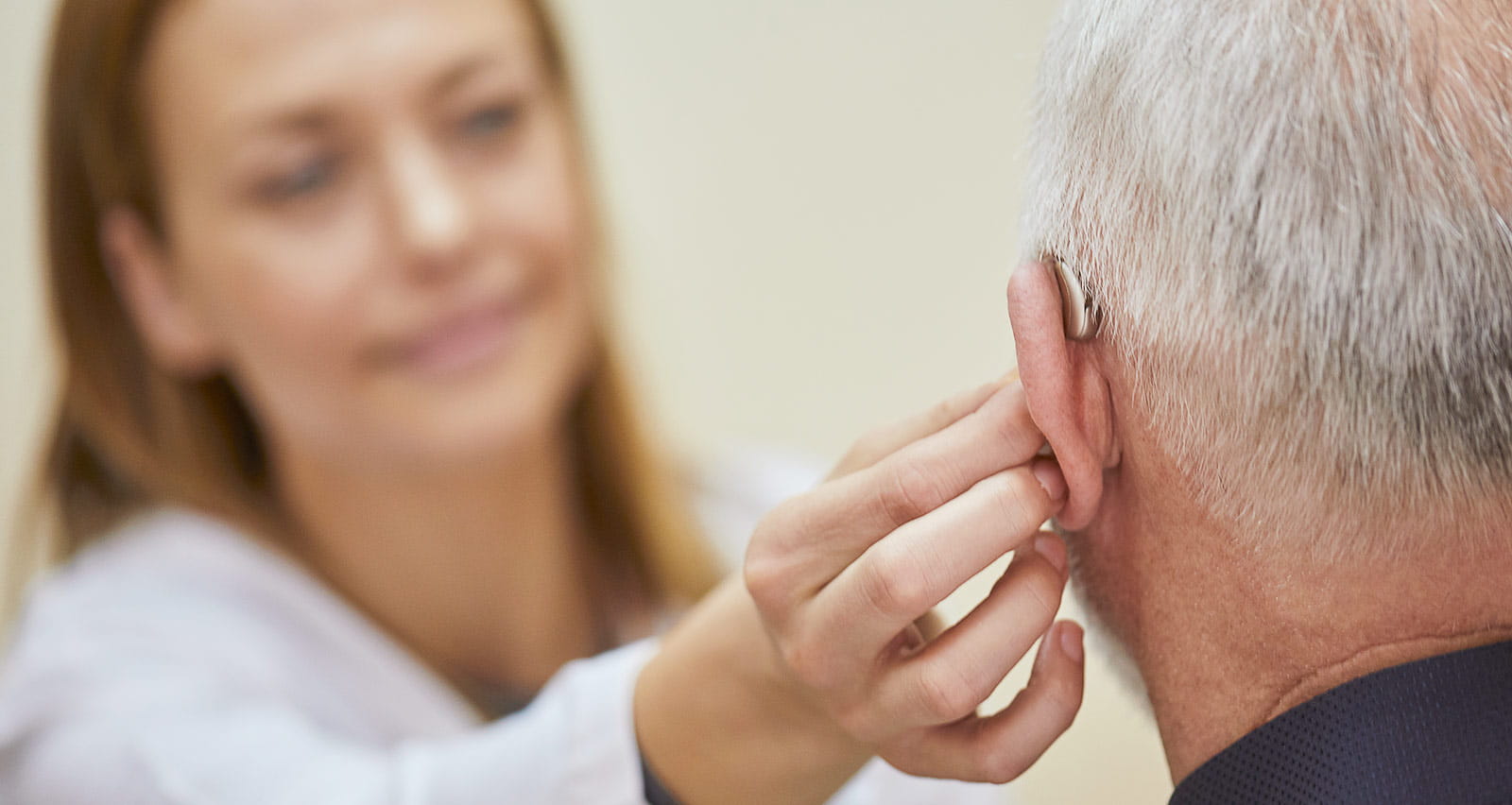 Female doctor applying hearing aid to senior man's ear